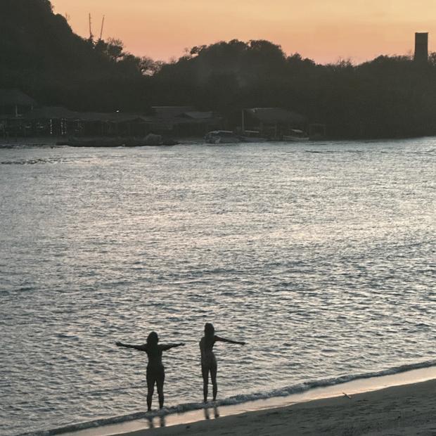 Dos mujeres de espaldas en la orilla del mar, con los brazos abiertos, al atardecer